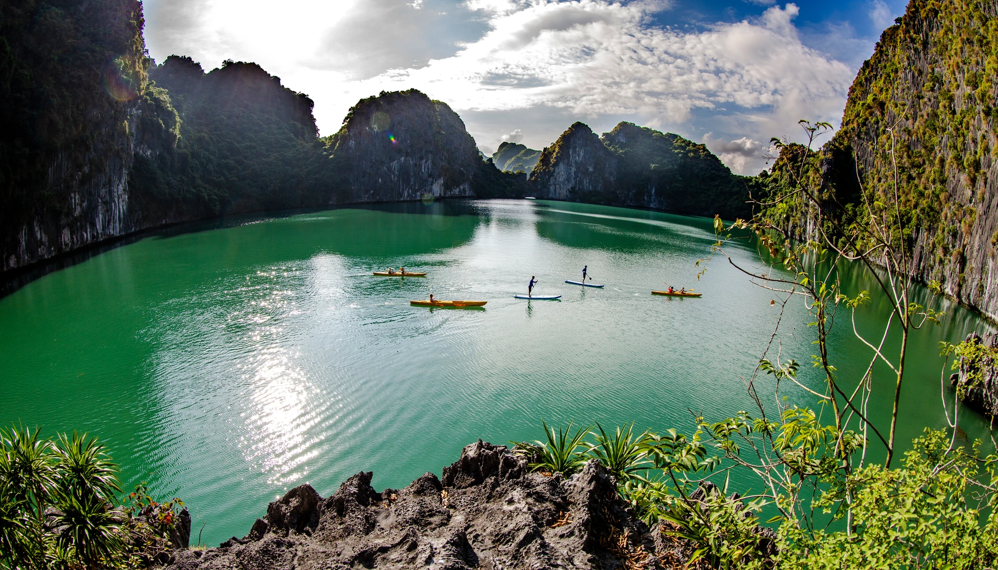 Kayaks and a paddleboard on sheltered green water among Lan Ha Bay limestone islands